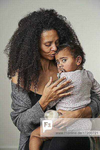 Curly haired woman carrying daughter on gray background
