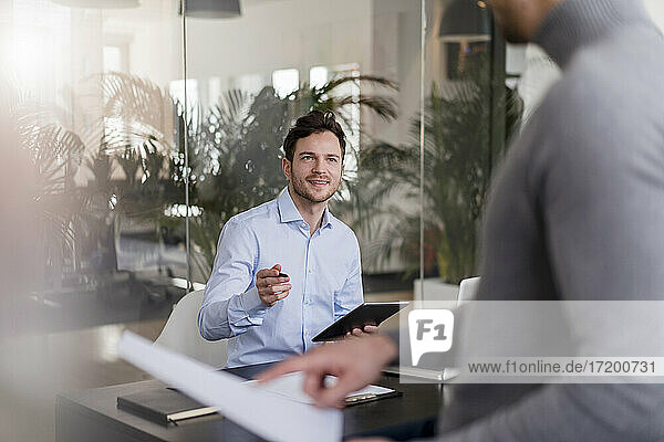 Businessman holding digital tablet discussing with male colleague in office