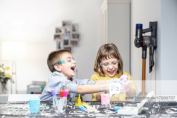 Cheerful brother and sister with slime on hands playing at table