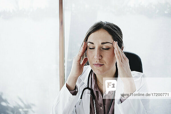 Overworked female doctor with head in hands