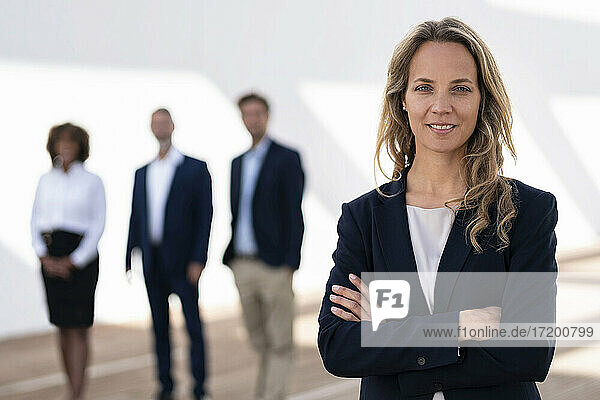 Mittlere erwachsene Geschäftsfrau stehend mit Kollegen im Hintergrund auf einer Büroterrasse