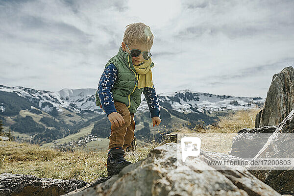 Boy with sunglasses climbing on rock against sky at Salzburger Land  Leogang Mountains  Austria