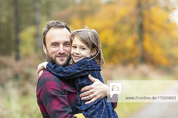 Lächelnde Tochter umarmt Vater im Wald stehend