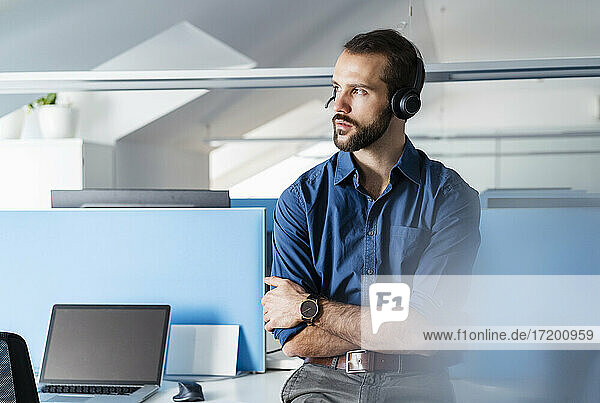 Entrepreneur wearing headphones sitting with arms crossed at office
