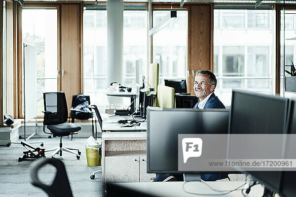 Lächelnder Geschäftsmann sitzt inmitten von Computern im Büro
