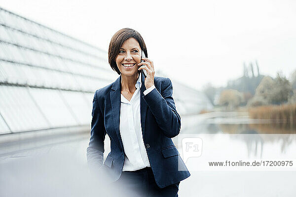 Lächelnde Geschäftsfrau  die außerhalb des Büros mit einem Smartphone spricht