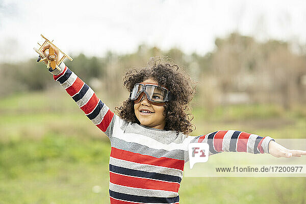 Lächelnder süßer Junge mit Fliegerbrille  der mit einem Holzspielzeugflugzeug spielt