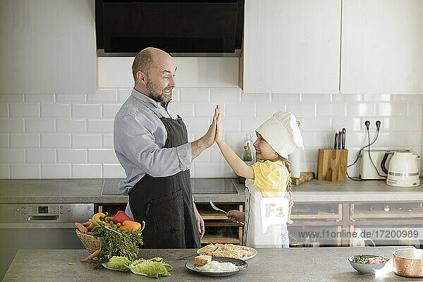 Mature men and girl cheering with giving high-five while standing in kitchen at home