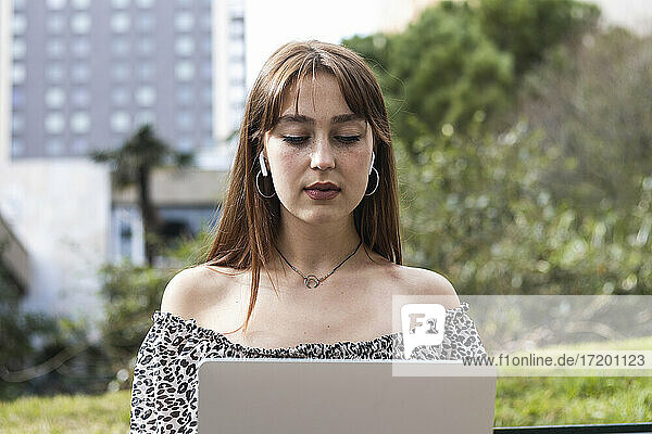 Geschäftsfrau mit In-Ear-Kopfhörern bei der Arbeit am Laptop