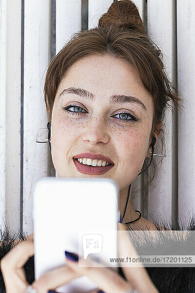 Schöne Frau mit blauen Augen hält Smartphone beim Hören von Musik auf Bank