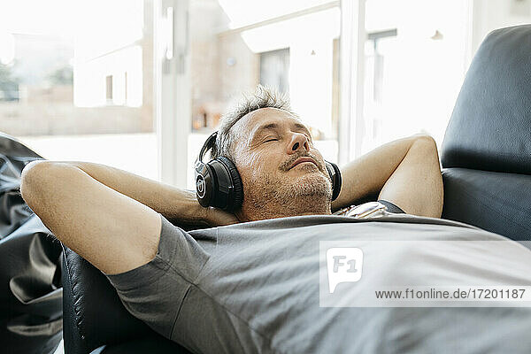 Mature man listening music through headphones while relaxing on sofa in living room