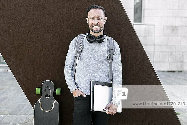 Smiling male entrepreneur with hand in pocket standing against wall