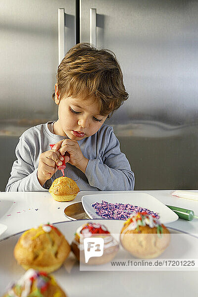 Cute boy decorating muffin at kitchen counter