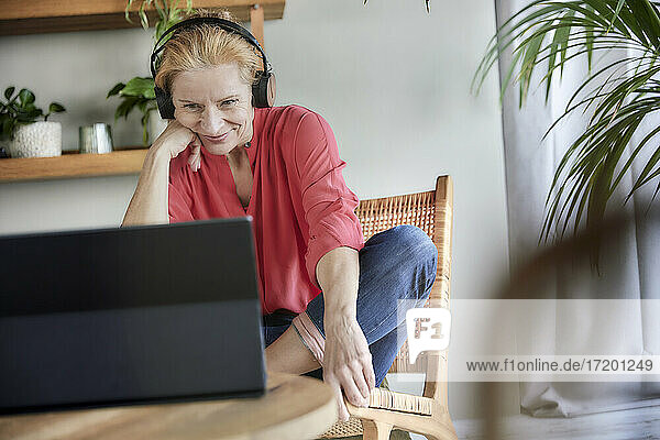 Frau mit Kopfhörern bei einem Videogespräch auf dem Laptop zu Hause
