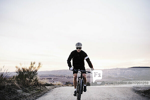 Männlicher Radfahrer fährt Fahrrad gegen den Himmel bei Sonnenuntergang