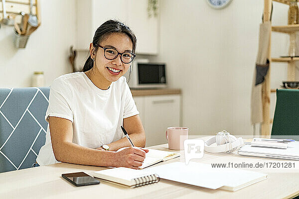 Lächelnde Frau mit Brille sitzt zu Hause bei einem Buch
