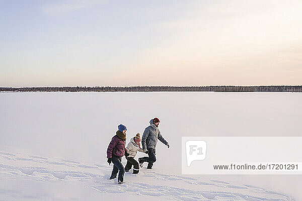Familie  die sich an den Händen hält  während sie im Winter auf Schnee gegen den Himmel läuft