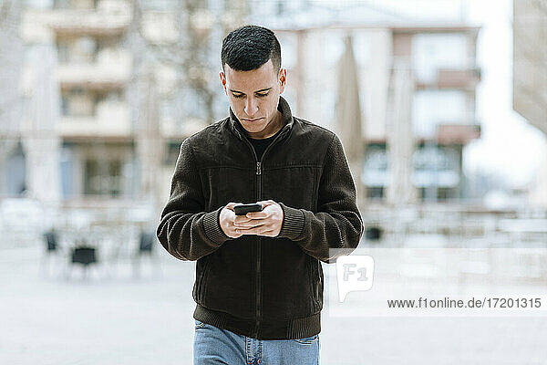 Junger Mann  der ein Handy benutzt  während er gegen ein Gebäude läuft