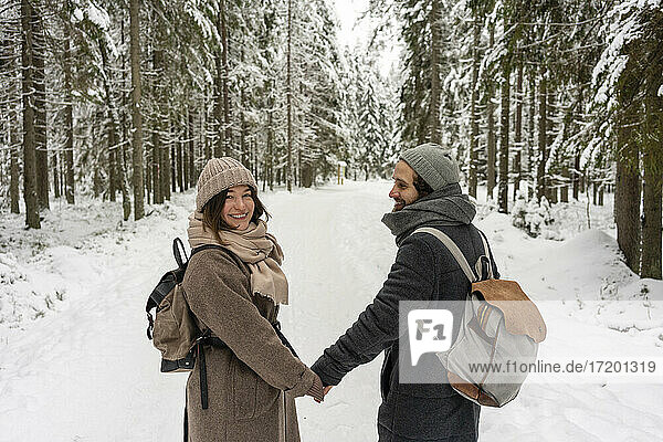 Young woman smiling while holding hand of man standing in forest