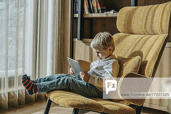 Junge beim E-Learning auf einem Stuhl im Wohnzimmer sitzend