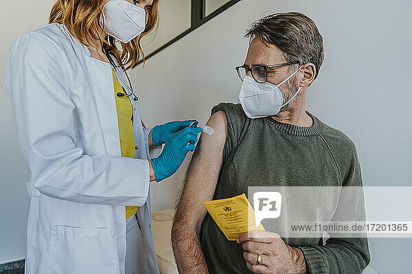 Eine Ärztin klebt einen Verband auf den Arm eines Patienten  während sie im Untersuchungsraum steht