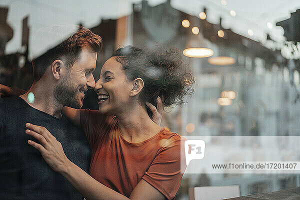Smiling couple rubbing noses while sitting by cafe window