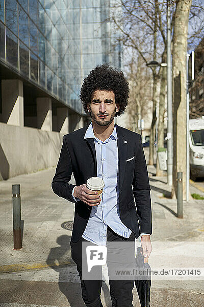 Gutaussehender Geschäftsmann mit Kaffeetasse auf der Straße an einem sonnigen Tag