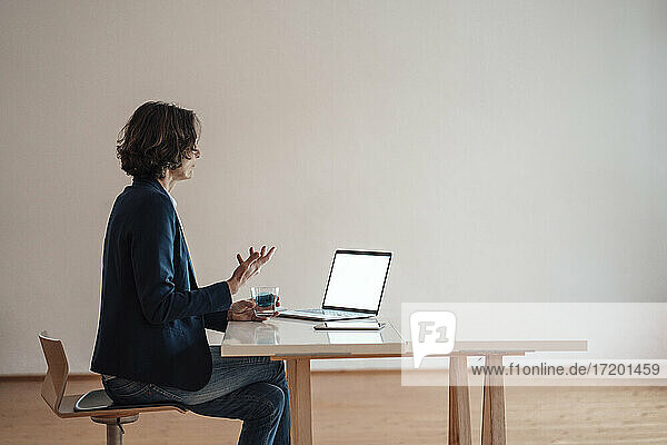 Frau gestikuliert bei der Verwendung eines Laptops auf dem Tisch im Büro zu Hause