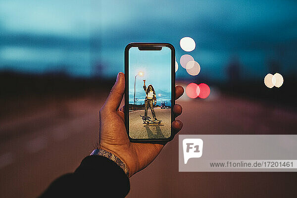 Young man photographing woman on skateboard during dusk