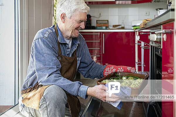 Lächelnder älterer Mann schiebt Gemüsefach in den Ofen
