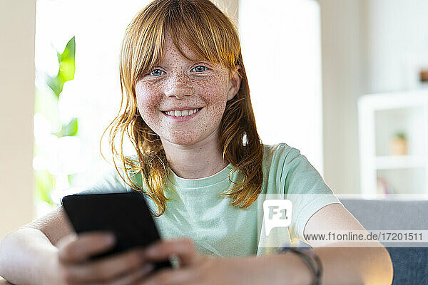 Nettes lächelndes rothaariges Mädchen hält Smartphone zu Hause