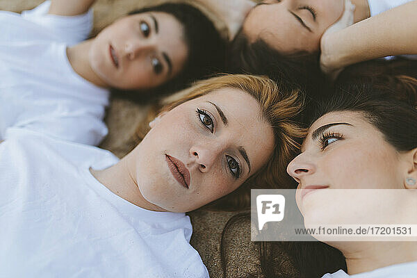 Female friends looking at blond woman while lying on sand