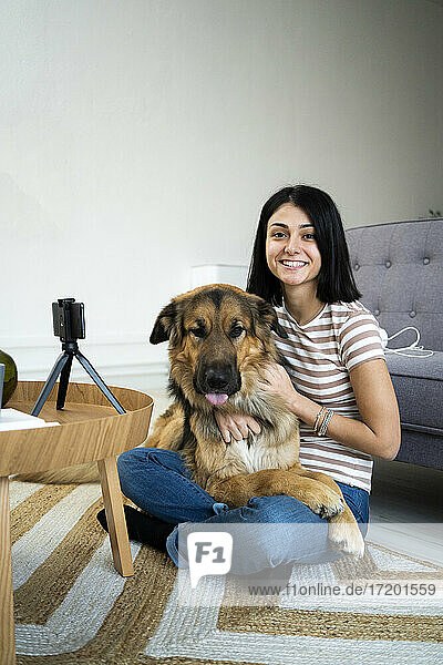 Lächelnde junge Frau mit Hund auf dem Schoß im Wohnzimmer