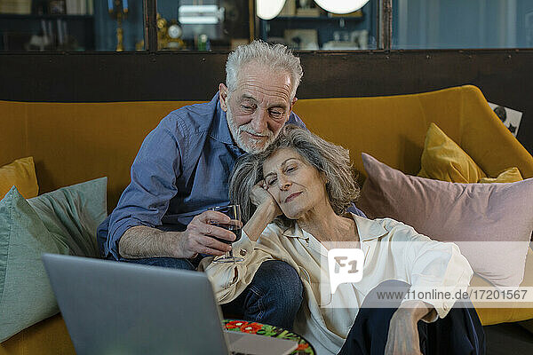 Älteres Ehepaar unterhält sich per Videoanruf auf dem Laptop  während es zu Hause auf dem Sofa sitzt