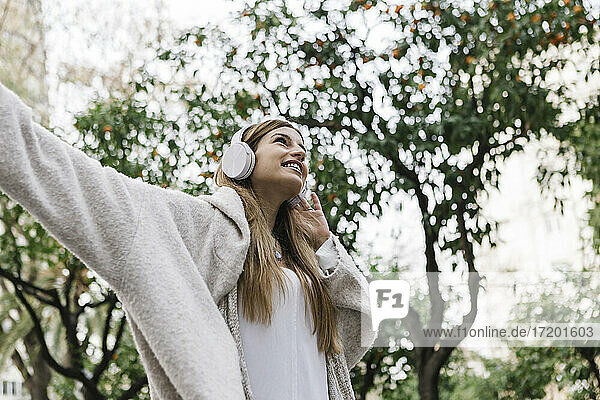 Junge Frau lächelt  während sie im Freien über Kopfhörer Musik hört