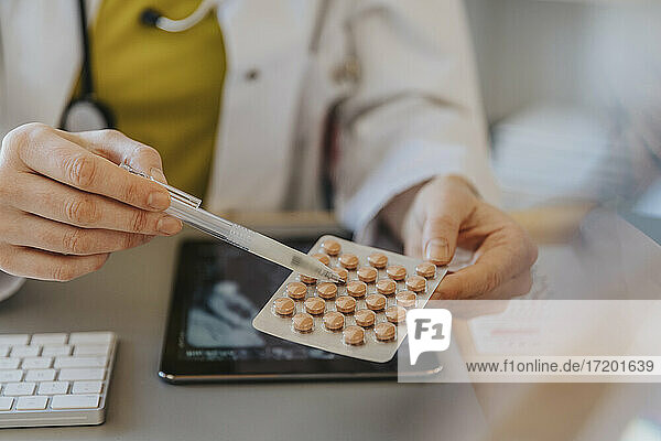 Arzt  der auf ein Medikament zeigt  während er am Schreibtisch in einer Klinik sitzt