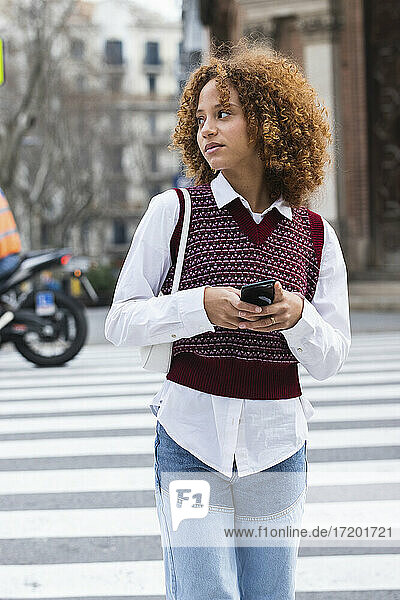 Weiblicher Teenager mit Mobiltelefon  der beim Überqueren der Straße wegschaut