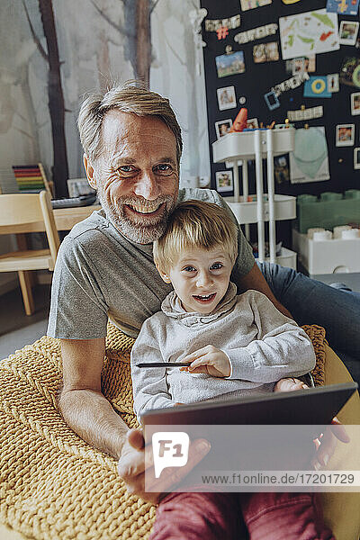 Lächelnder Vater und Sohn mit digitalem Tablet im Schlafzimmer