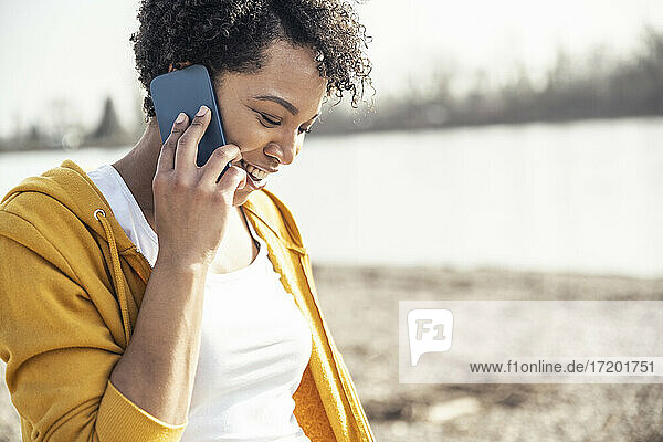 Lächelnde Frau  die im Freien an einem sonnigen Tag mit ihrem Handy spricht