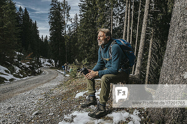 Smiling mature man looking away while holding water bottle against trees at Salzburger Land  Austria