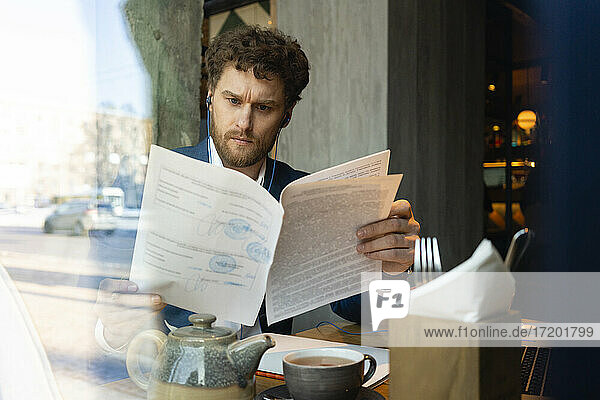 Männlicher Unternehmer prüft Strategie  während er im Café sitzt  gesehen durch Glas