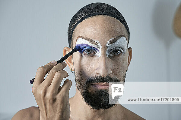 Mid adult man applying blue eyeshadow with make-up brush on eye
