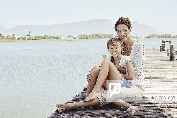 Smiling mother and boy sitting on pier during sunny day
