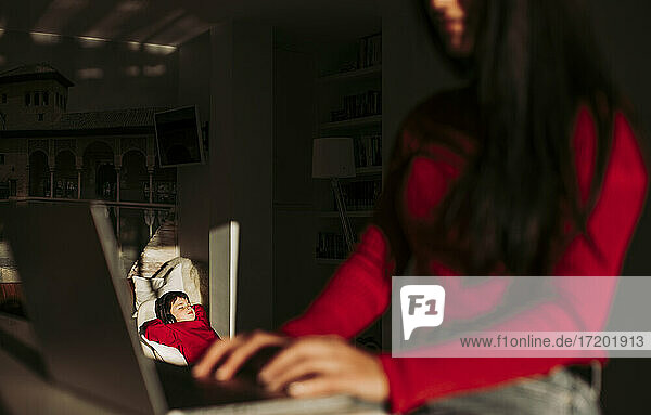 Junge hört Musik  während die Mutter zu Hause am Laptop arbeitet