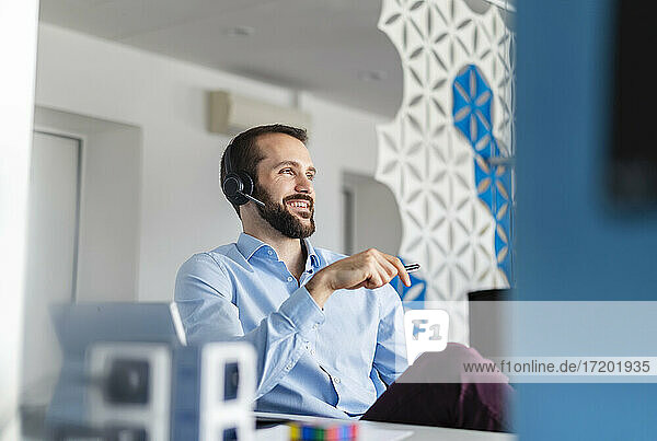 Nachdenklicher Unternehmer mit Kopfhörern  der lächelnd im Büro sitzt