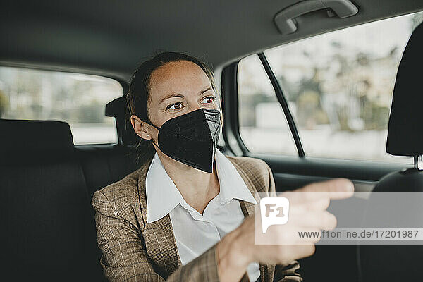 Weibliche Fachkraft mit Gesichtsmaske gestikuliert während der Fahrt im Taxi während COVID-19