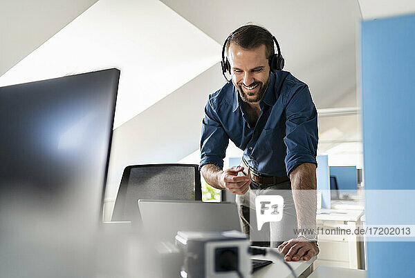 Lächelnde Fachkraft  die über Kopfhörer einen Videoanruf über einen Laptop im Büro führt