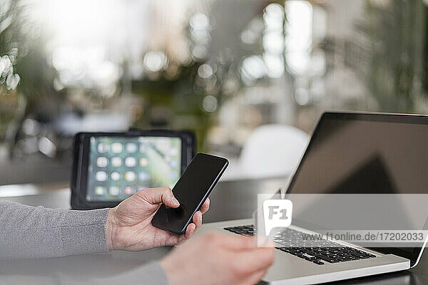 Die Hände eines männlichen Unternehmers beim Online-Bezahlen mit einer Kreditkarte auf einem Smartphone im Büro