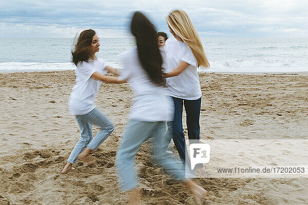 Junge Freundinnen laufen im Kreis  während sie in den Ferien am Strand spielen