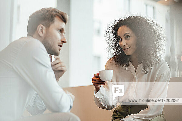 Geschäftsfrau mit Kaffeetasse hört einem Kollegen zu  während sie in einem Café sitzt